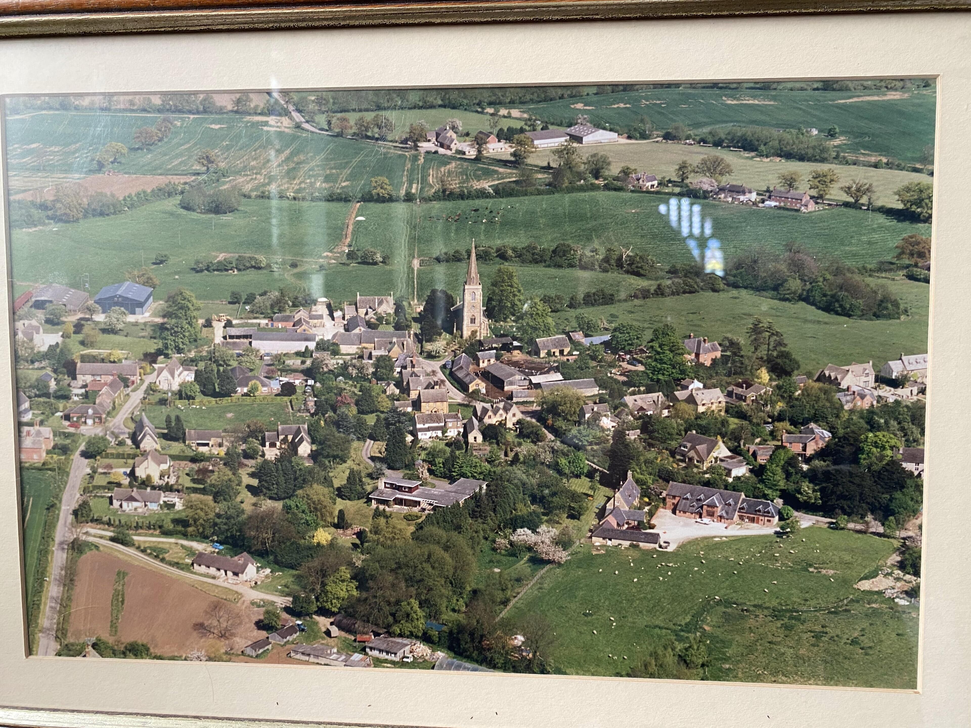 An aerial view of a village with a prominent church, scattered houses, and green fields.