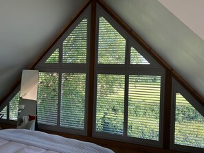A bedroom with a sloped ceiling, large windows with blinds, a bed, and a bedside table with a lamp. - Fabulous Barn in Great Wolford, Moreton in Marsh (Shipston on Stour)