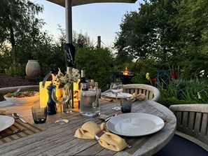 An outdoor dining table set with plates, glasses, and a pitcher of water, surrounded by greenery and a decorative vase. - Fabulous Barn in Great Wolford, Moreton in Marsh (Shipston on Stour)