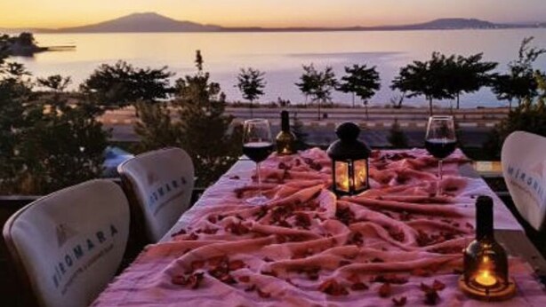 Una mesa dispuesta para dos, con vista al mar y montañas al fondo.
