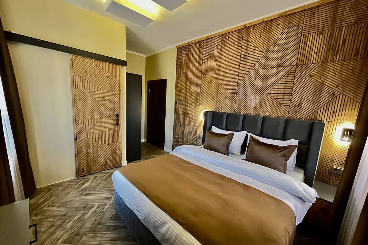 A modern hotel room with a large bed, wooden panel wall, and a herringbone floor pattern.