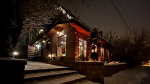 Un edificio cubierto de nieve con fachada de piedra y vigas de madera, iluminado por una cálida luz interior.