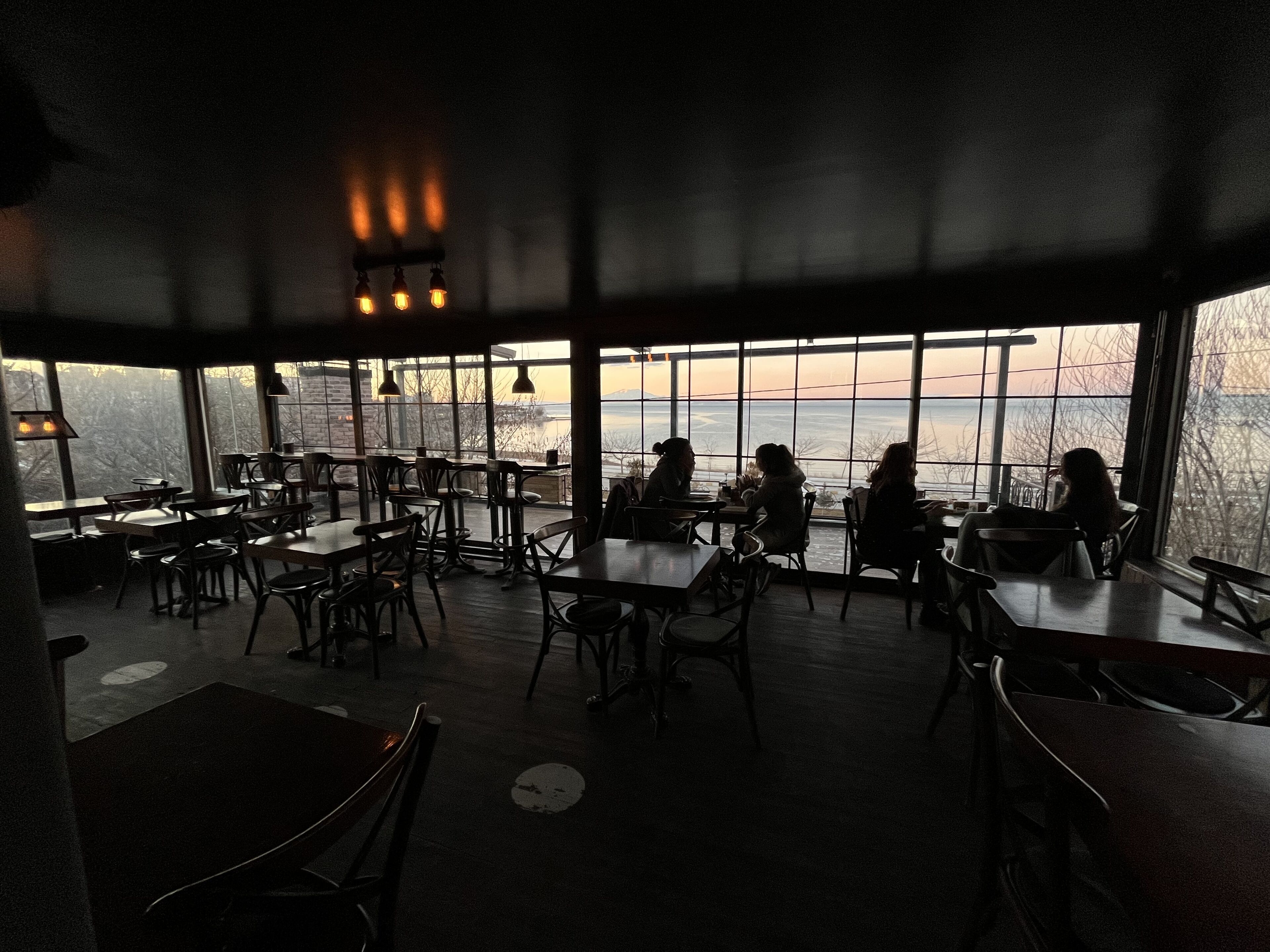 Un espace de restauration intérieur avec des tables et des chaises, et de grandes fenêtres donnant sur l’extérieur.