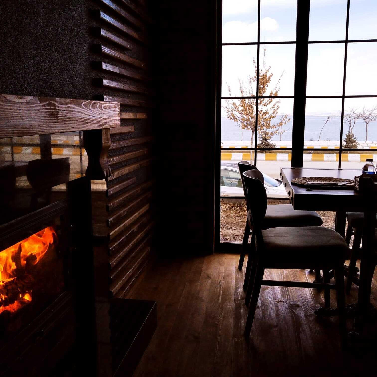 A room with a fireplace, a table with chairs, and a view of the outside.