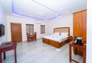 A modern hotel room with a wooden bed, a desk, a chair, and a coffee maker.