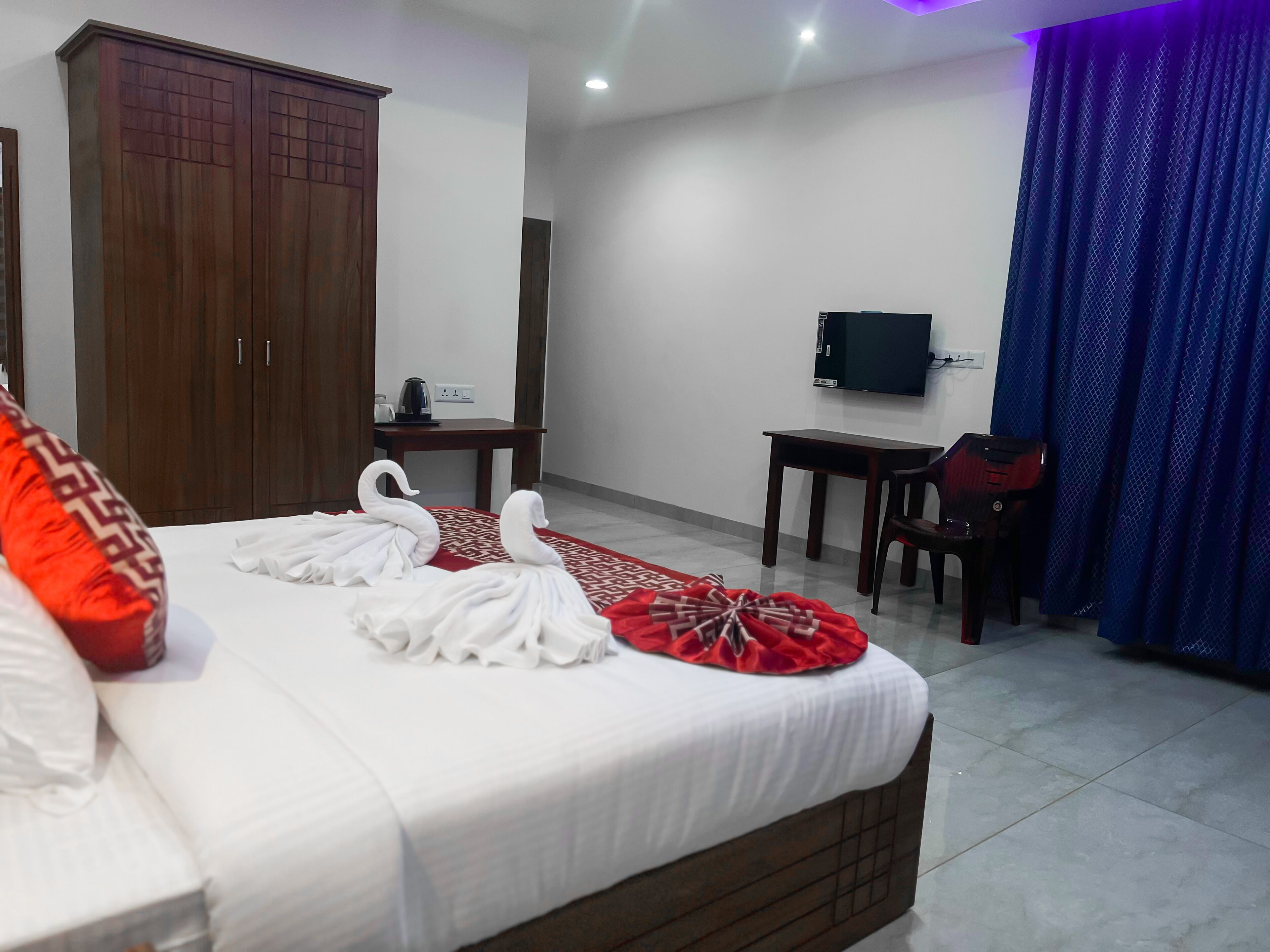 Habitación de hotel con cama, armario, escritorio, silla, televisor y cortina.