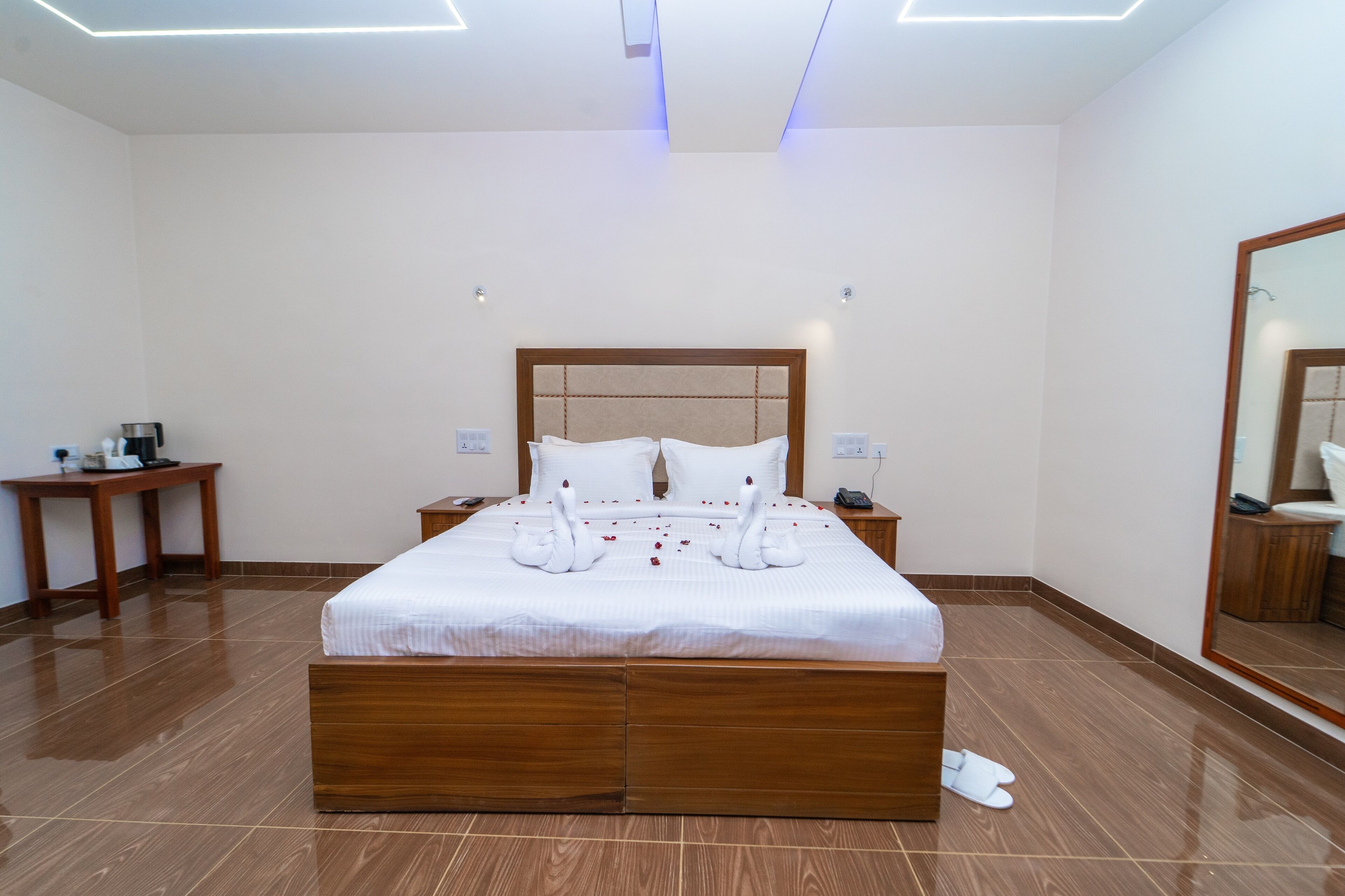 Una habitación de hotel con una cama grande, cabecero de madera, mesitas de noche y un espejo.