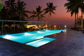 A swimming pool with a tiled deck, surrounded by palm trees and a sunset in the background. - Skylar Seaview Beach Resort and Spa (Varkala)