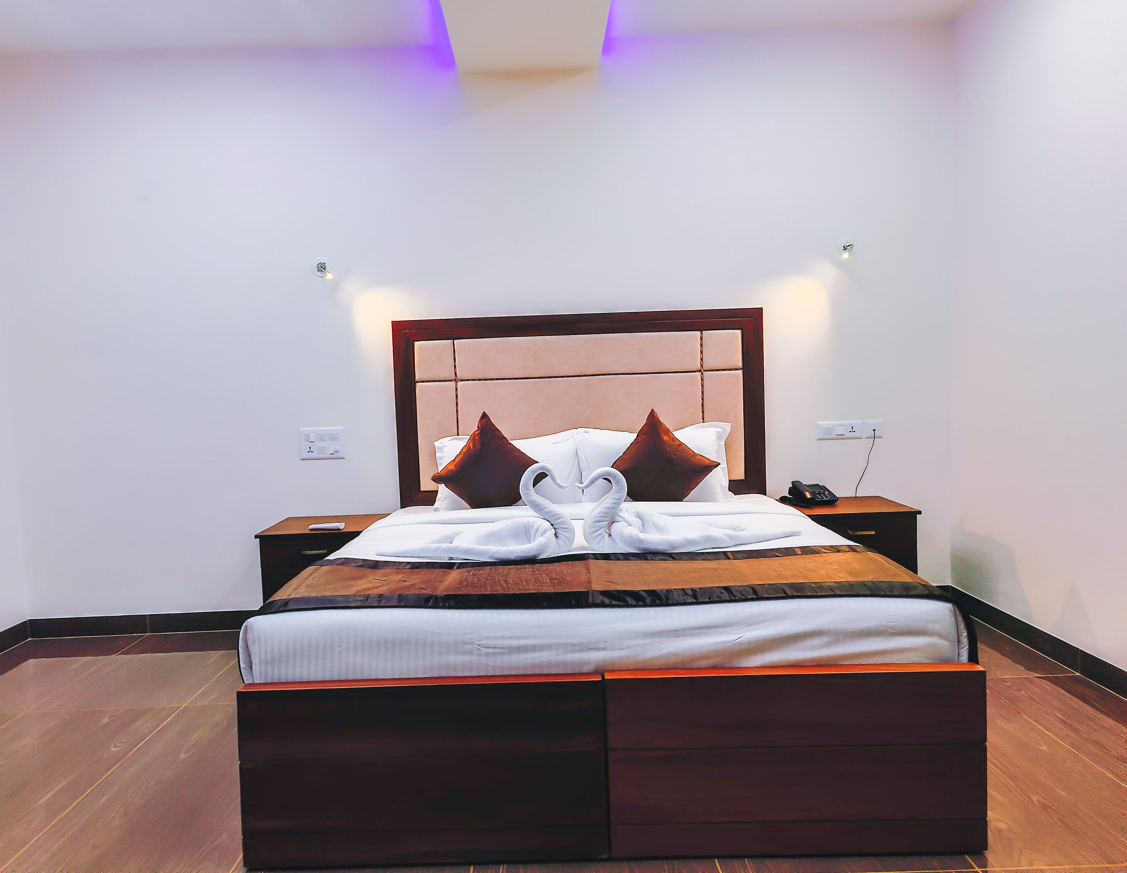 A neatly made bed with a wooden headboard, two bedside tables, and a wall socket.