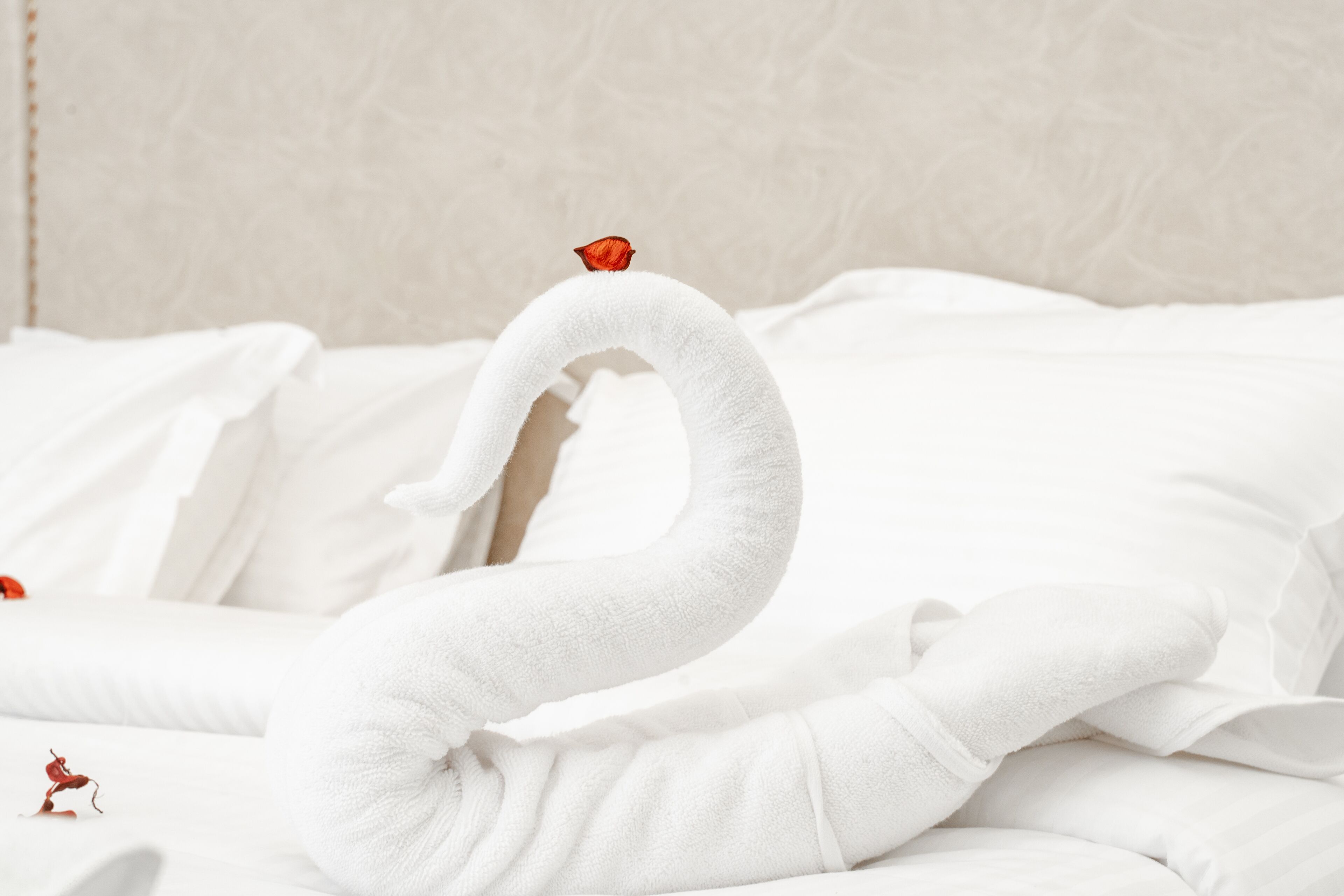A bed with a white swan-shaped towel and a small red decoration.
