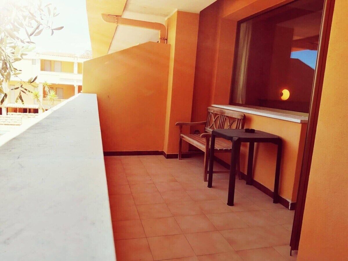 Ein Balkon mit einer Holzbank und einem Tisch, ein Fenster mit Blick auf den Sonnenuntergang und ein gefliester Boden.