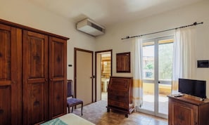 A bedroom with a bed, wooden wardrobe, a chair, a dresser, a television, and a sliding glass door leading to an outdoor area. - Club Malaspina Hotel & Resort (Bosa)