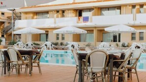 A poolside area with wicker chairs and umbrellas, a pool, and a building with balconies. - Club Malaspina Hotel & Resort (Bosa)