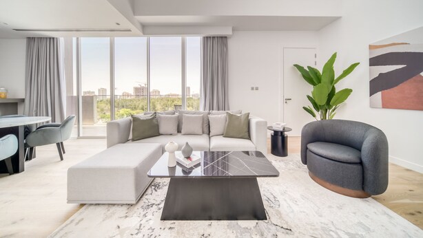 A modern living room with a sectional sofa, a coffee table, and a view of the city. - Al Barari Stella Stays (Dubai)