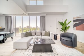 A modern living room with a sectional sofa, a coffee table, and a view of the city. - Al Barari Stella Stays (Dubai)