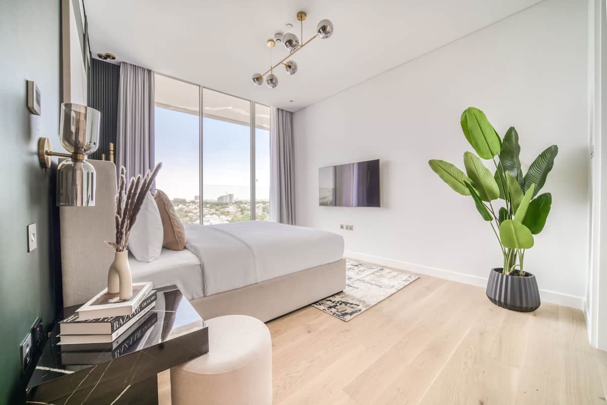 Un dormitorio moderno con una cama grande, un televisor, una planta en maceta y vistas a la ciudad.