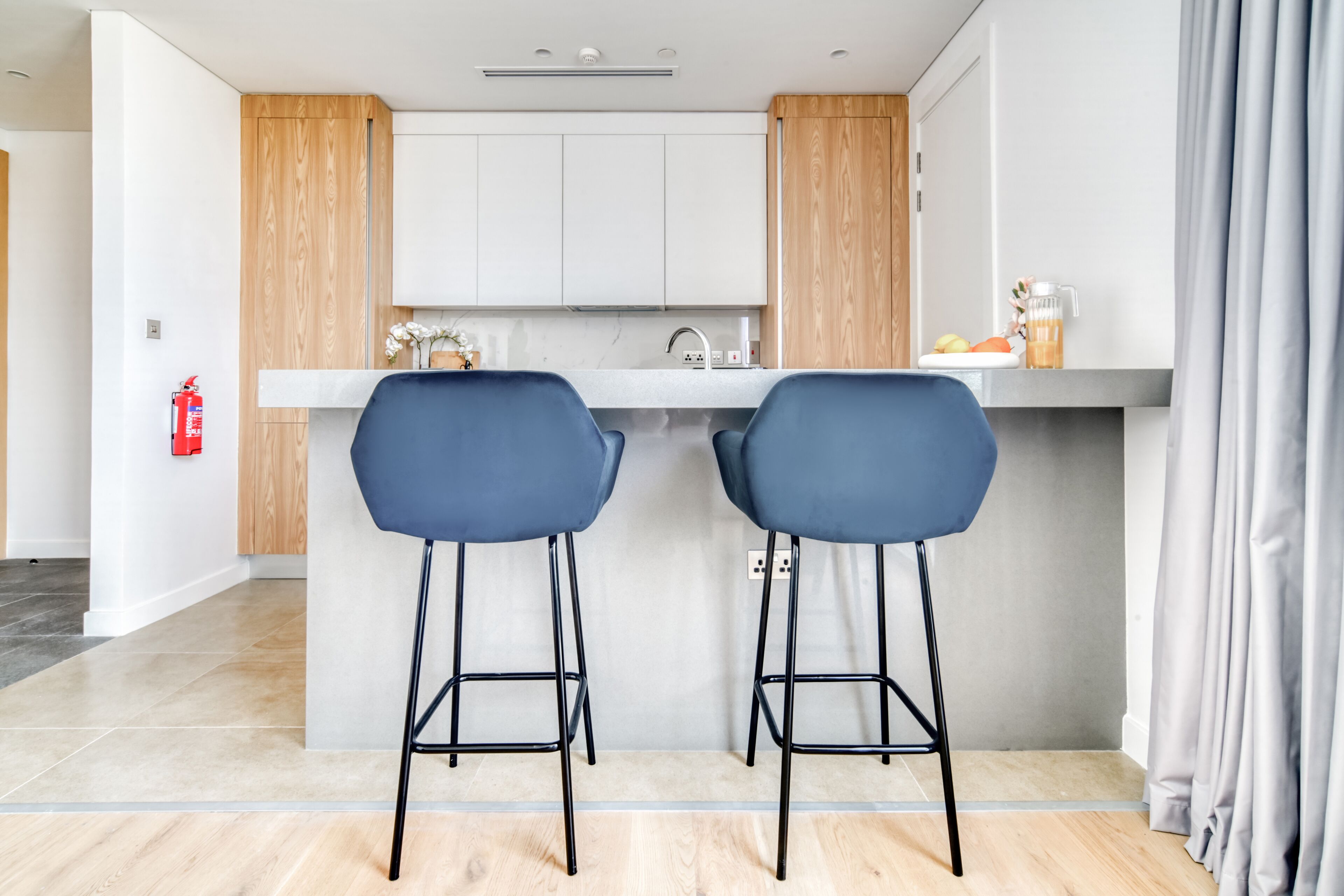 Una cocina moderna con dos taburetes azules, una encimera blanca y armarios de madera.