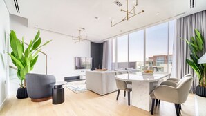 A modern living room with a dining area, large windows, and a flat-screen TV. - Al Barari Stella Stays (Dubai)