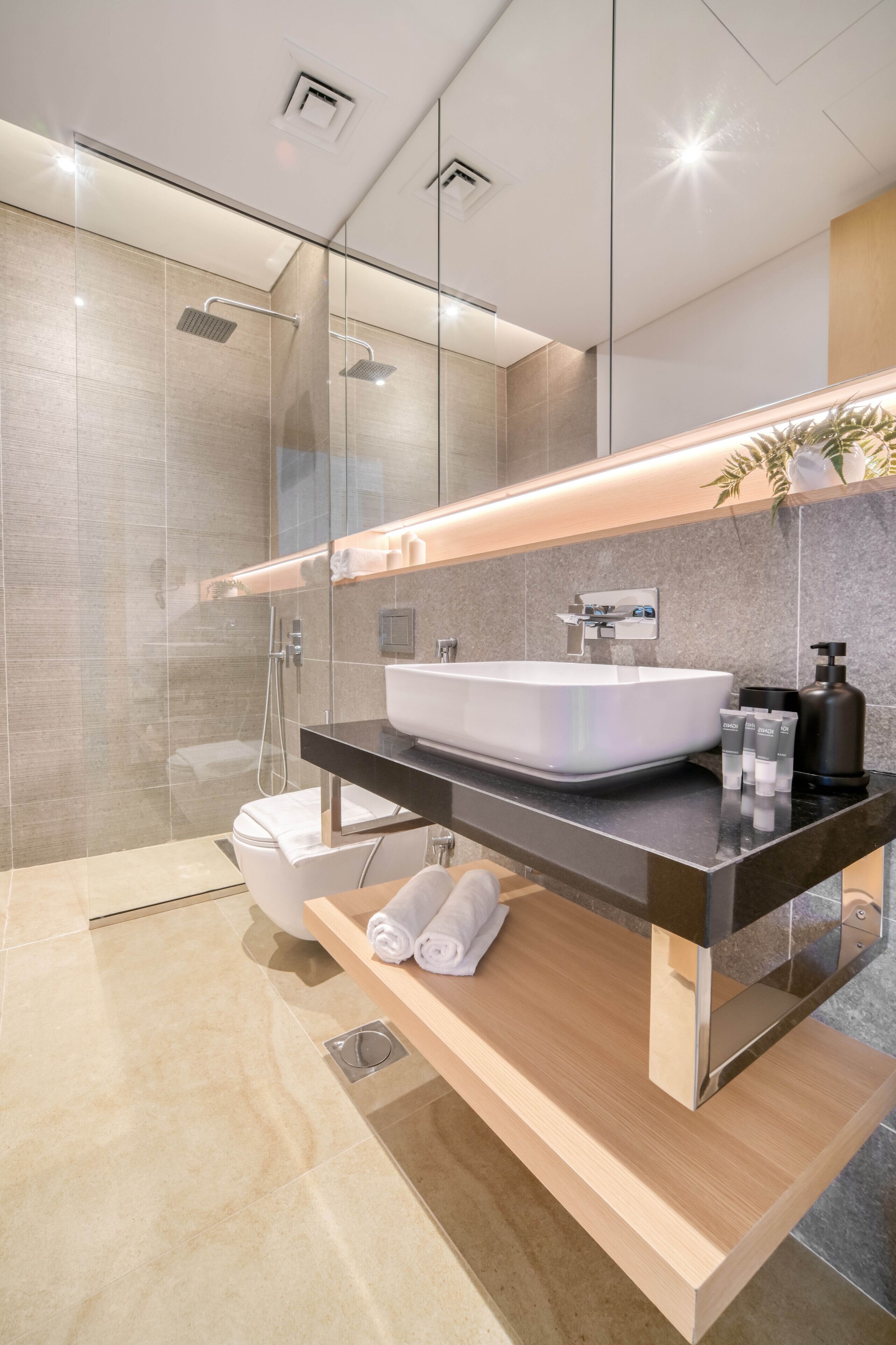 A modern bathroom with a glass-enclosed shower, a white sink, and a wooden vanity.