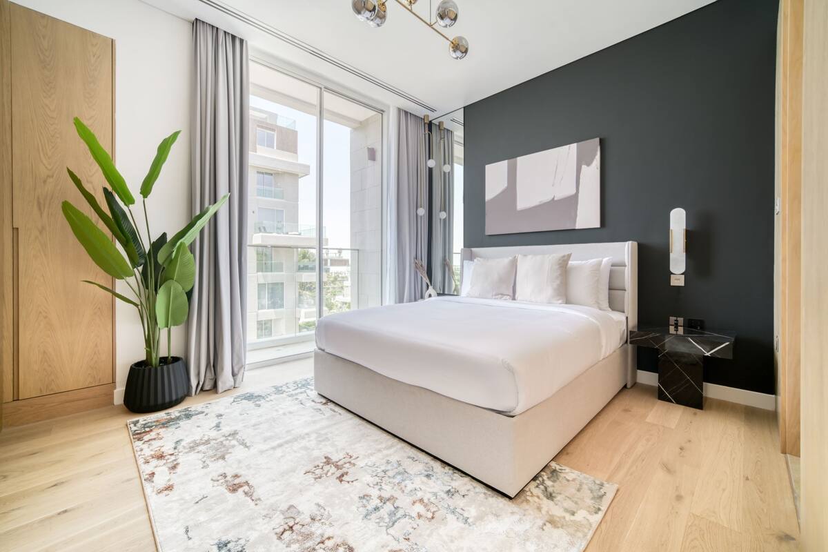 Un dormitorio moderno con una cama grande, una planta en maceta y vistas de la ciudad a través de amplios ventanales.