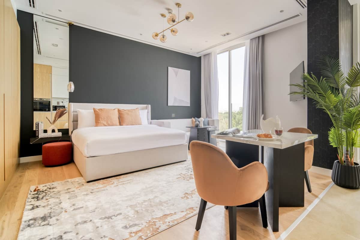 Una habitación de hotel moderna con una cama grande, una mesa de comedor, una silla, una planta en maceta y vistas a la ciudad.