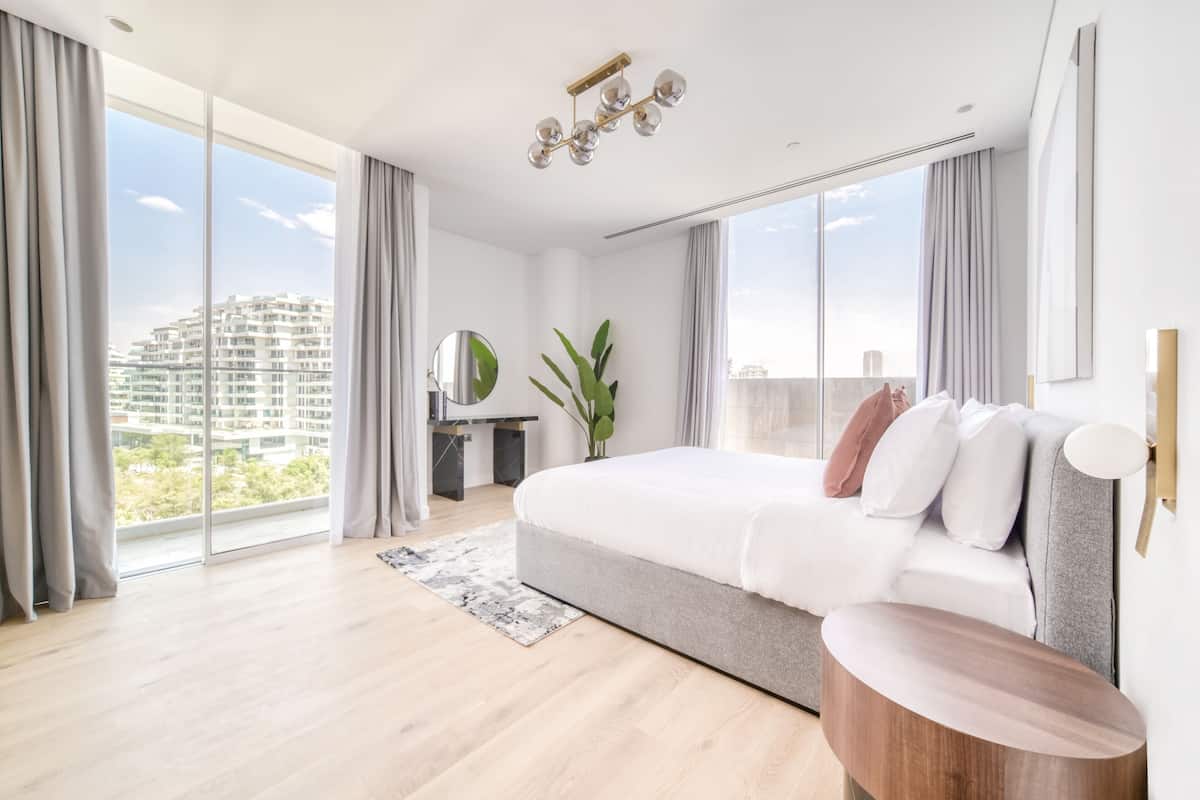 Un dormitorio moderno con una cama grande, un escritorio y vistas a un edificio de oficinas.