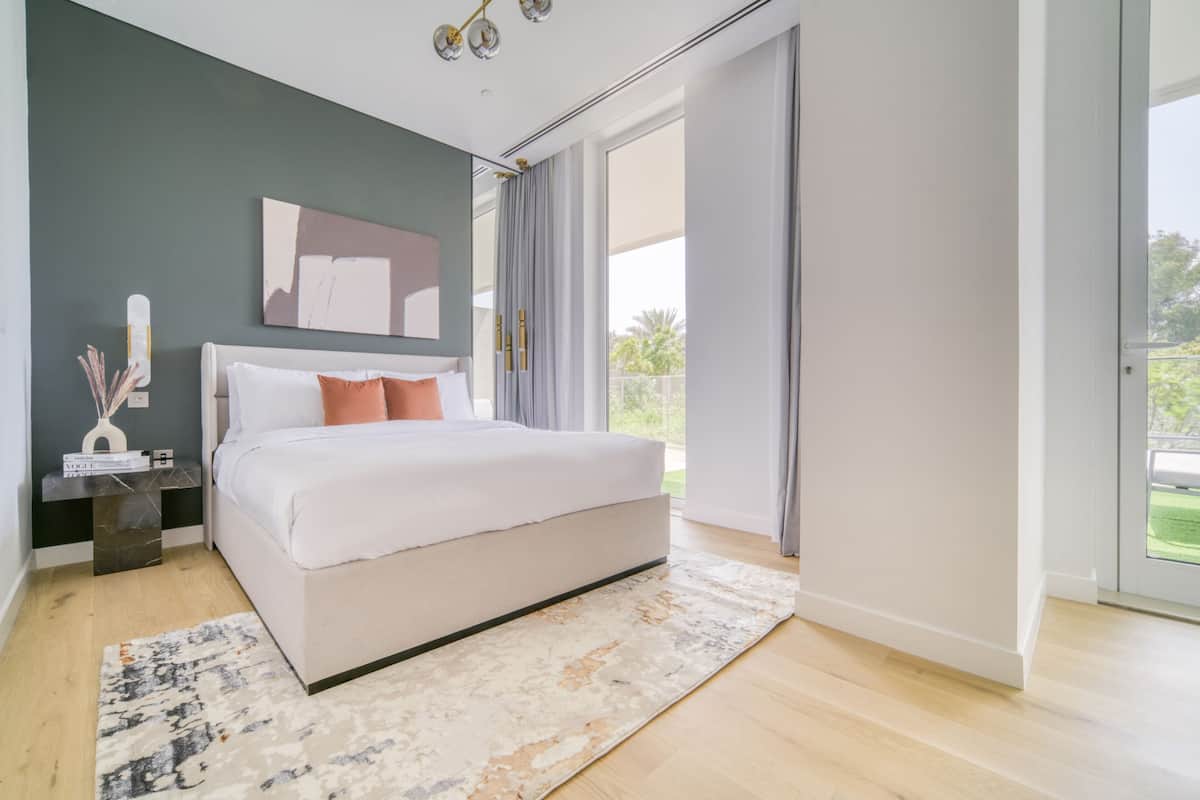 Un dormitorio moderno con una cama grande, una mesita de noche, un florero decorativo y vistas al exterior a través de una puerta corrediza.
