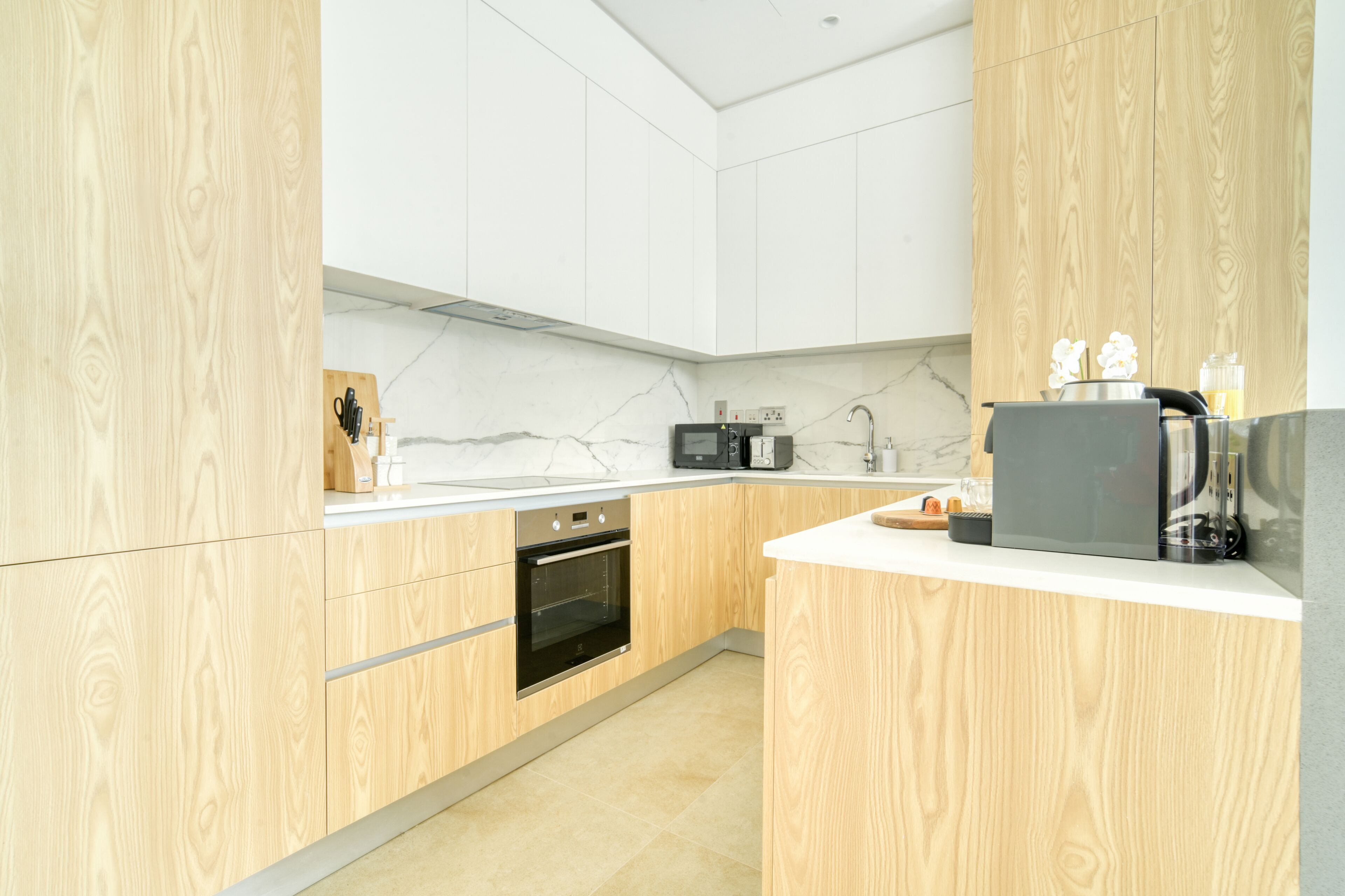 A modern kitchen with wooden cabinets, a built-in oven, a microwave, and a coffee machine.