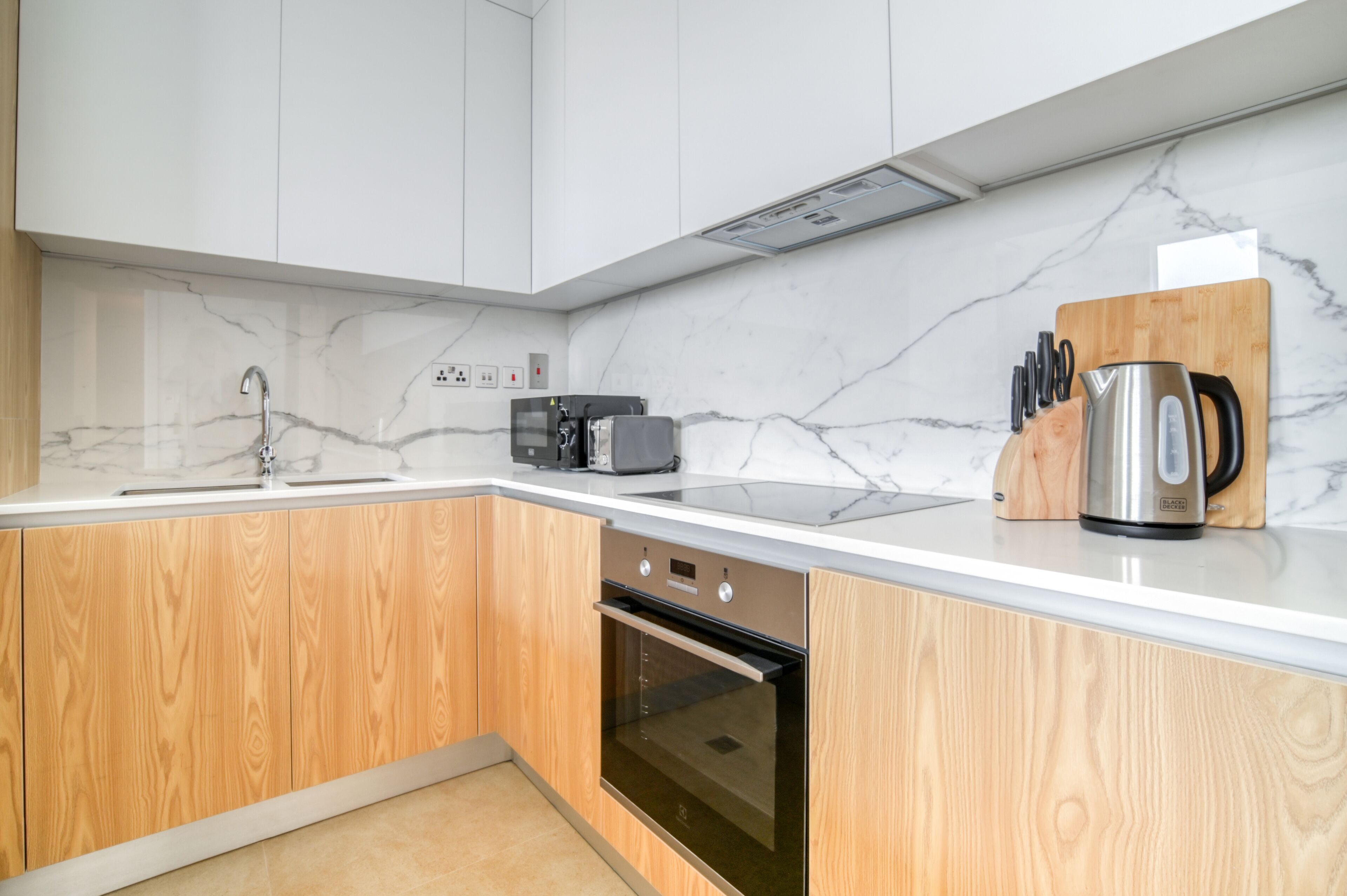Una cocina moderna con encimeras de mármol blanco, armarios de madera, horno empotrado y cafetera.