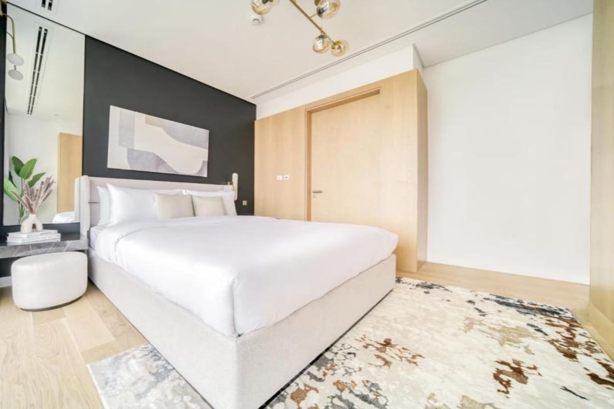A modern bedroom with a large bed, a bedside table, a mirror, and a view of the outdoors.
