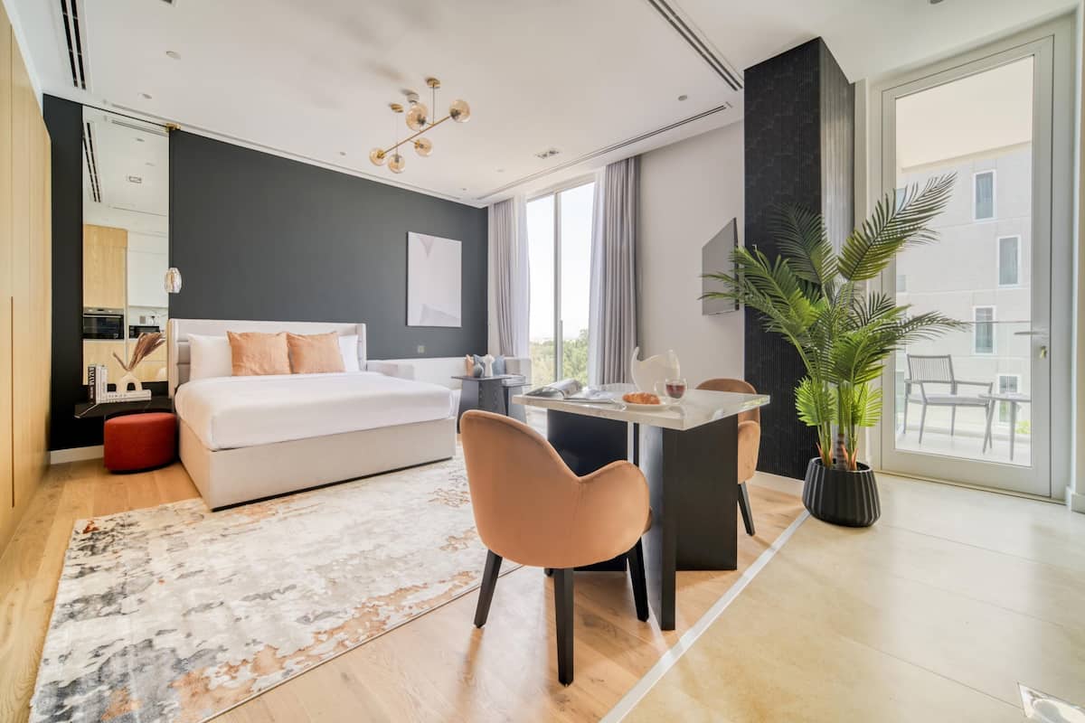 Una habitación de hotel moderna con una cama grande, una zona de comedor, un ventanal amplio y una planta en maceta.