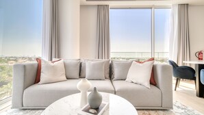 A modern living room with a grey sofa, white cushions, a marble coffee table, and a book. - Al Barari Stella Stays (Dubai)