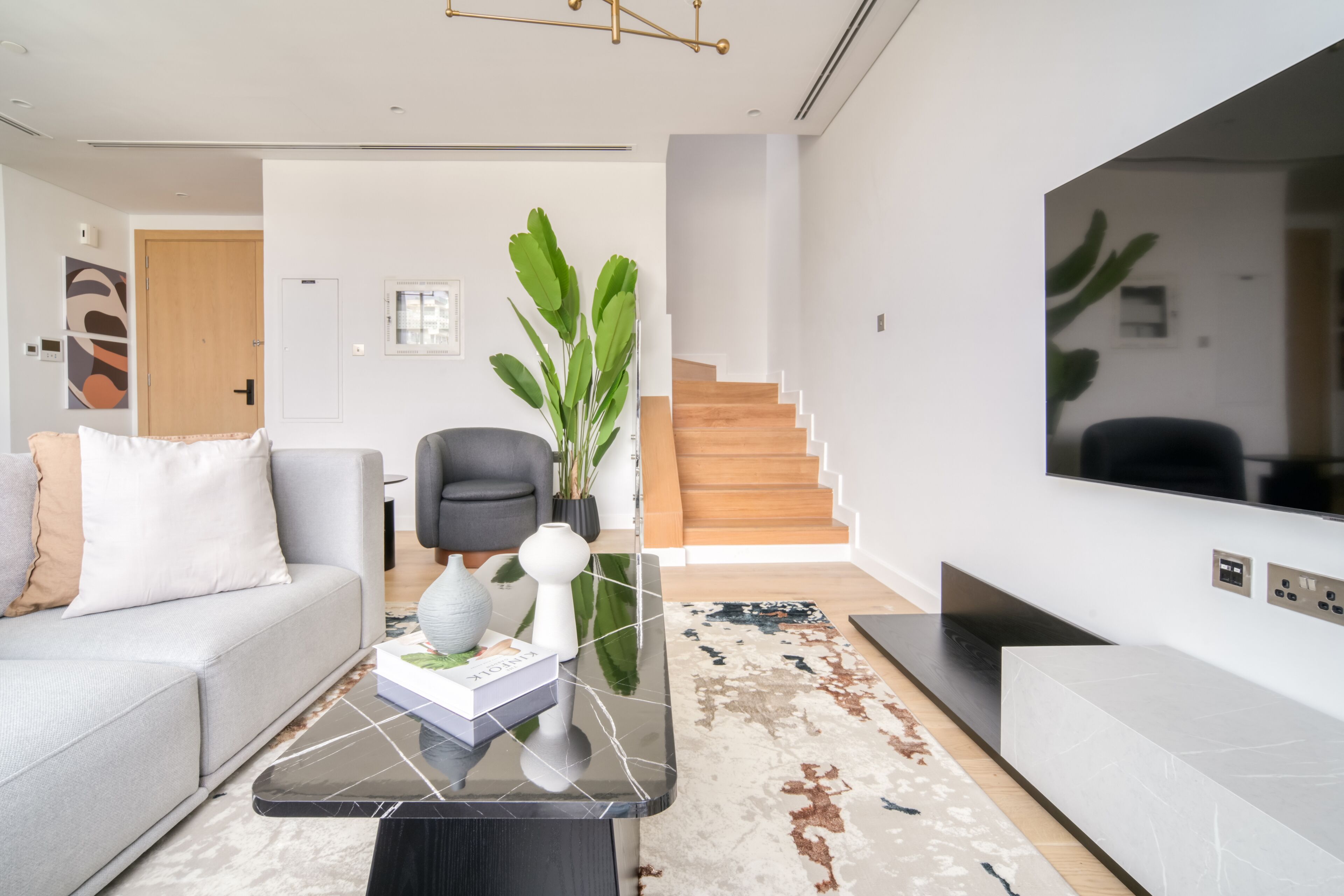 Ein modernes Wohnzimmer mit einer Couch, einem Couchtisch und einem großen Fernseher. Eine Treppe führt zu einer weiteren Ebene.