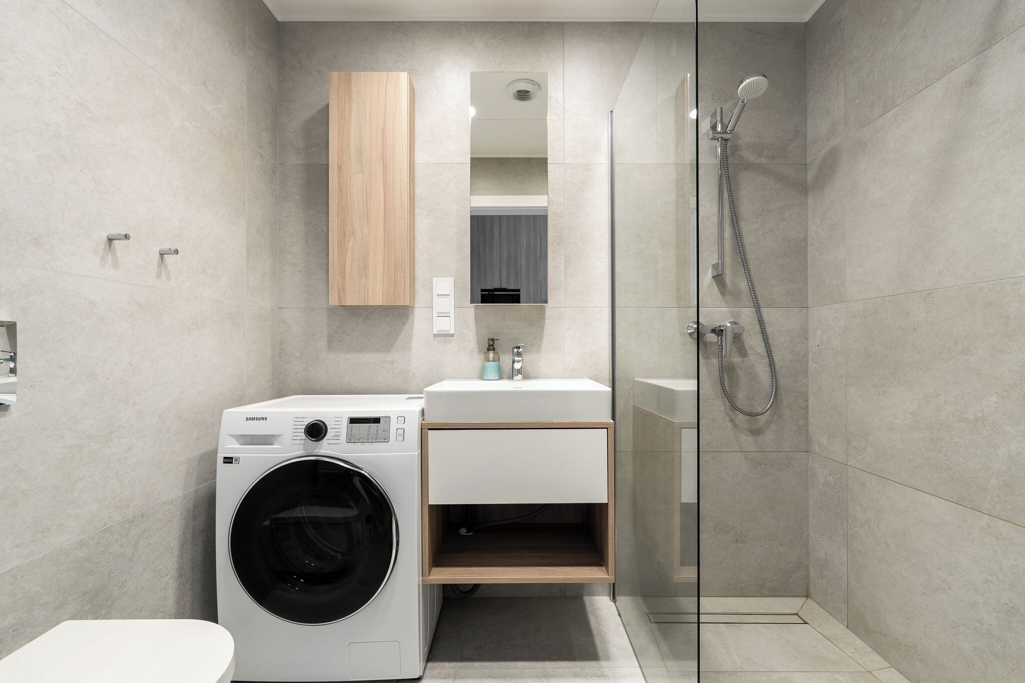 A modern bathroom with a washing machine, a sink, and a glass-enclosed shower.