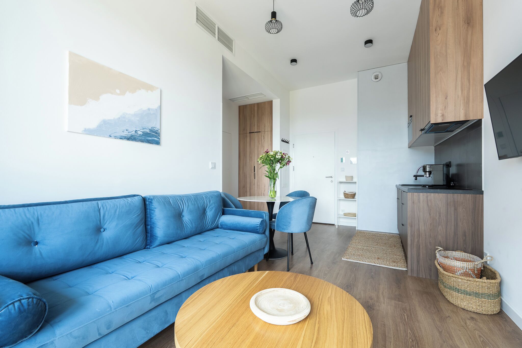 Ein modernes Wohnzimmer mit einem blauen Sofa, einem runden Couchtisch und einer Küchenzeile mit Holdekor und einer schwarzen Arbeitsplatte.