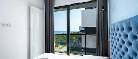 Un dormitorio moderno con una cama grande, vista al mar y un cabecero tapizado en azul.