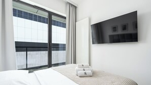 Habitación de hotel con cama, televisor, ventana con cortinas y vista al balcón exterior.