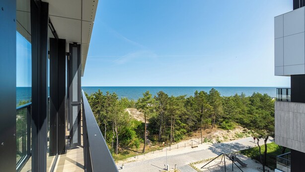 Un edificio moderno con amplios ventanales que dan a una playa y un bosque.