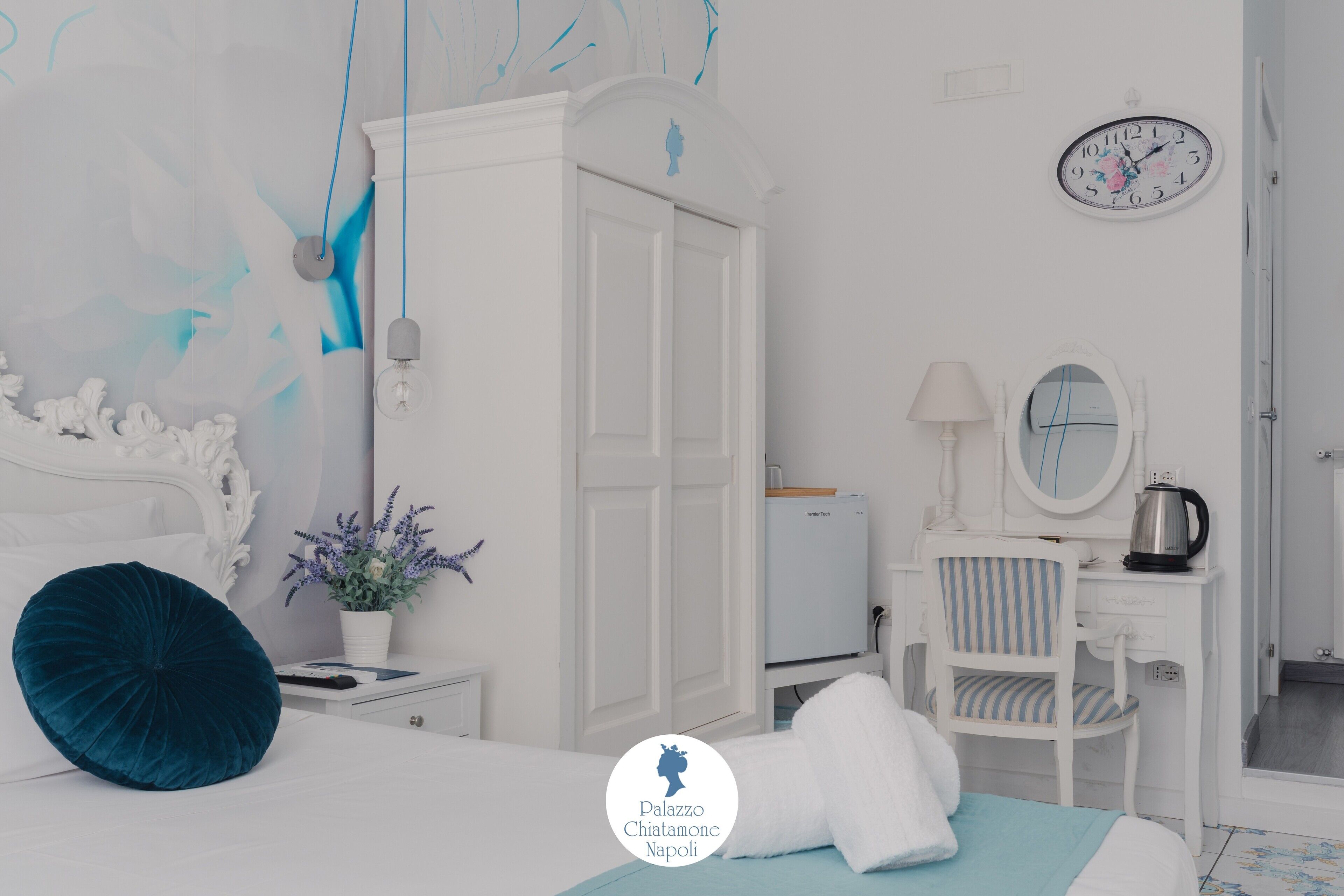 Un dormitorio con cama, mesita de noche, cómoda, silla, escritorio, reloj y un muro con diseño floral.