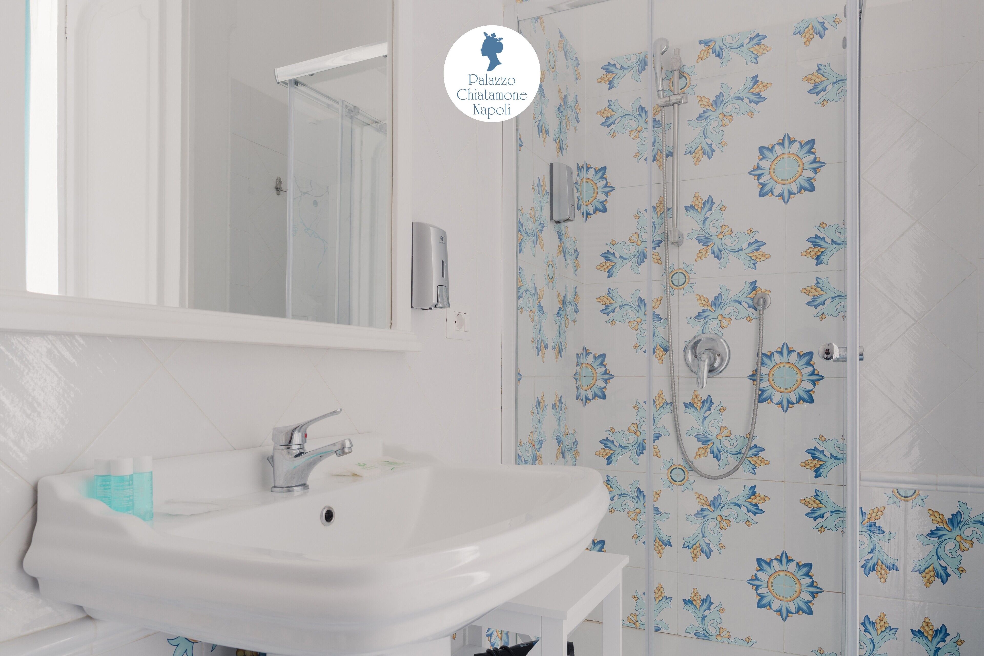Une salle de bain avec un lavabo blanc, un miroir et une douche ornée de carreaux à motifs floraux.