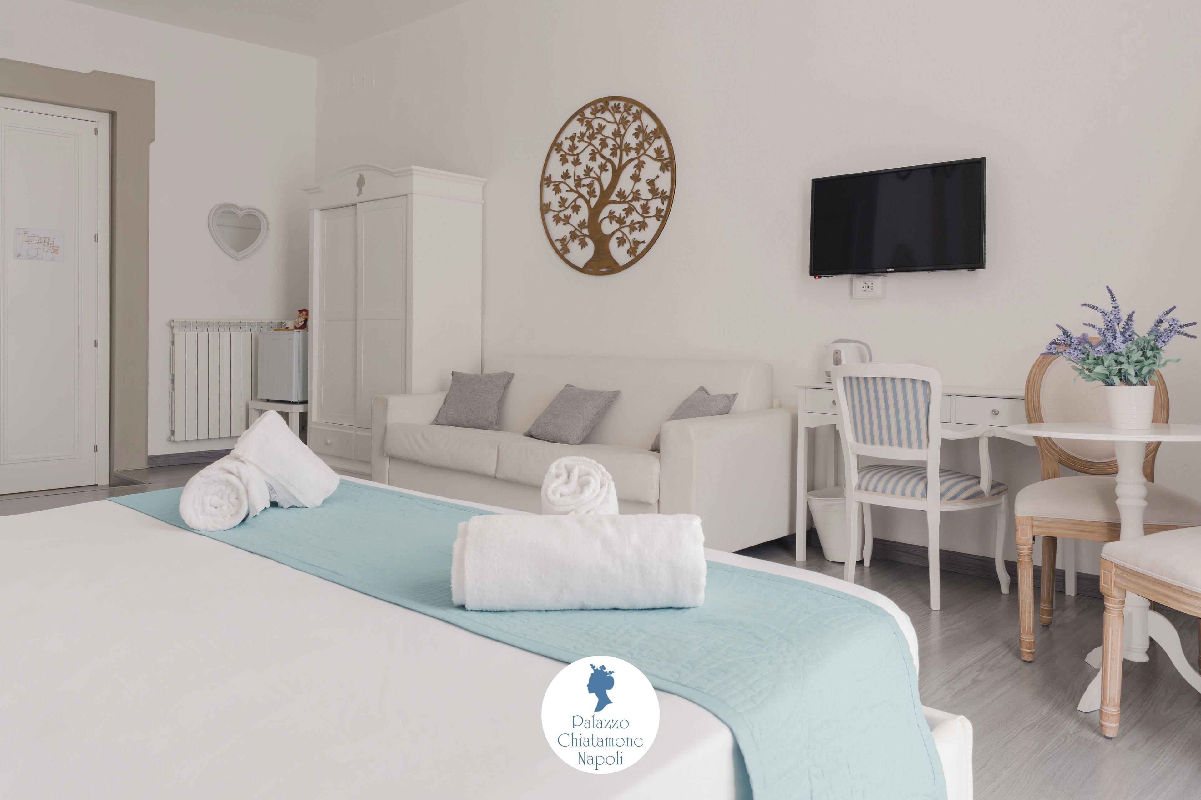 Une chambre d’hôtel moderne, équipée d’un lit, d’un bureau, d’une télévision et ornée d’un décor en forme de cœur au mur.
