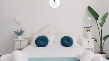 A neatly arranged bedroom with a white bed, two blue pillows, white bedside tables, and a potted plant.