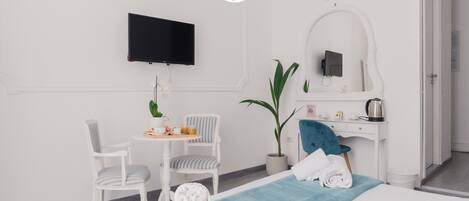 A hotel room with a bed, a desk, a chair, a TV, and a potted plant.