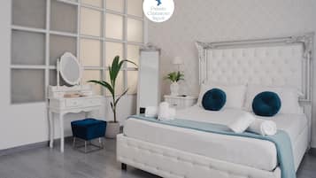 A bedroom with a large window, a white bed, a vanity with a mirror, and a potted plant.