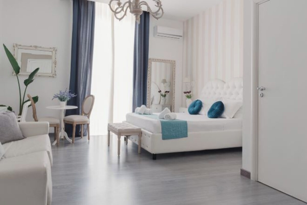 A modern bedroom with a white bed, blue pillows, a small table, and a chair.