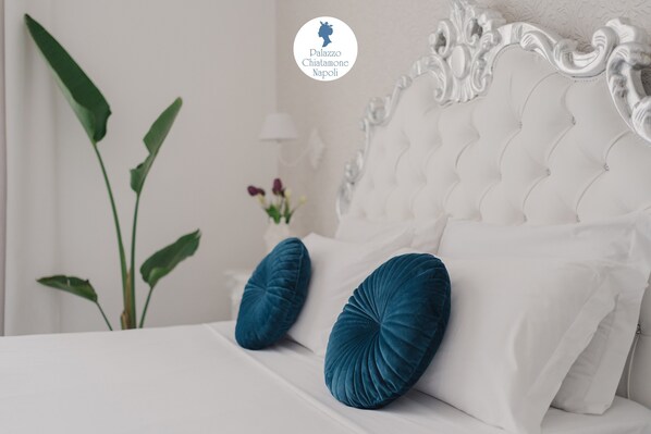 A bed with white bedding and two blue pillows, a white ornate headboard, and a green plant in the background.