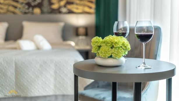 A hotel room with a bed, a small round table with a vase of flowers and two wine glasses. - Villa Solaris (Rewal)