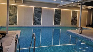 An indoor swimming pool with clear blue water, a glass ceiling, and marble wall panels. - Villa Solaris (Rewal)