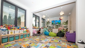 A children's playroom with a colorful alphabet carpet, play shelves, a slide, and a television. - Villa Solaris (Rewal)