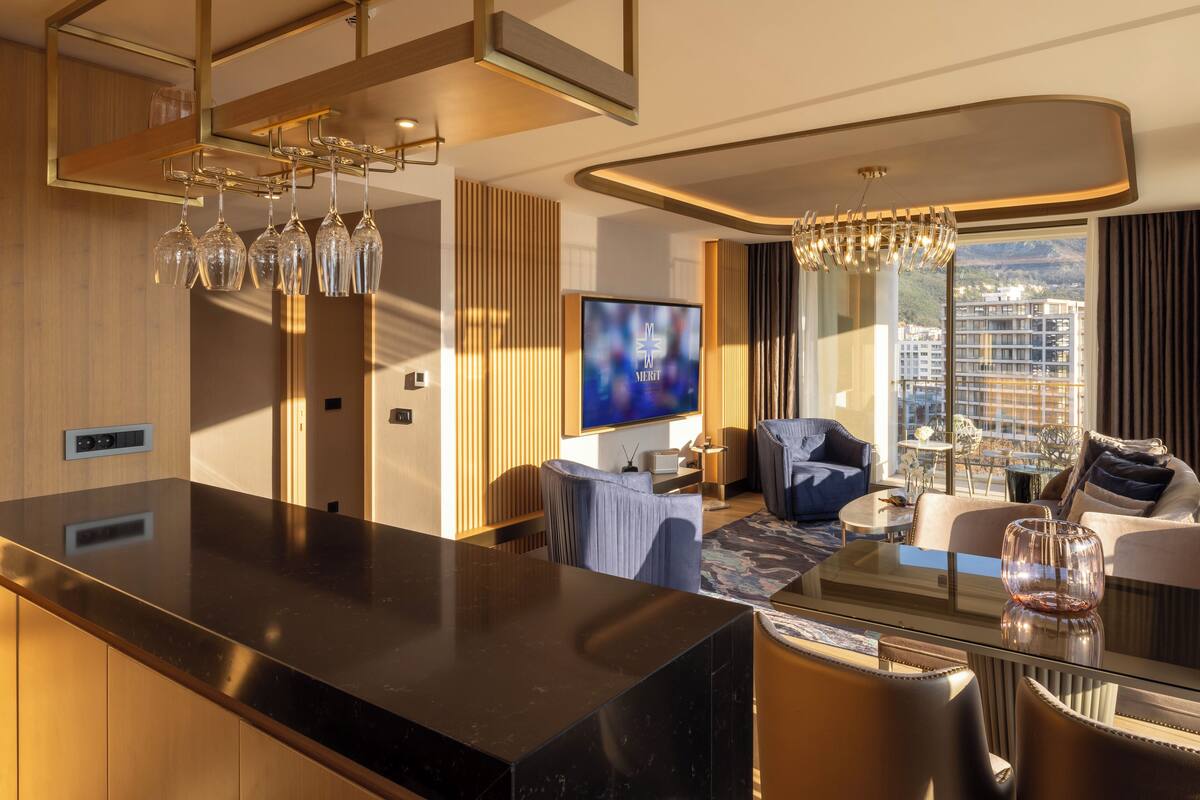 Une chambre d’hôtel moderne dotée d’une grande télévision, d’un coin repas avec une table en verre et offrant une vue sur la ville.